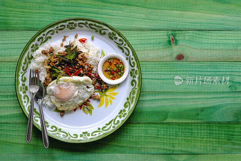 著名的泰国辣菜“Pak Krapao Moo”，英文中是用圣罗勒炸猪肉，在一张古老的绿色风化木餐桌上，用蒸饭、煎蛋和“Pik Nam Bla”(鱼酱辣椒)搭配。